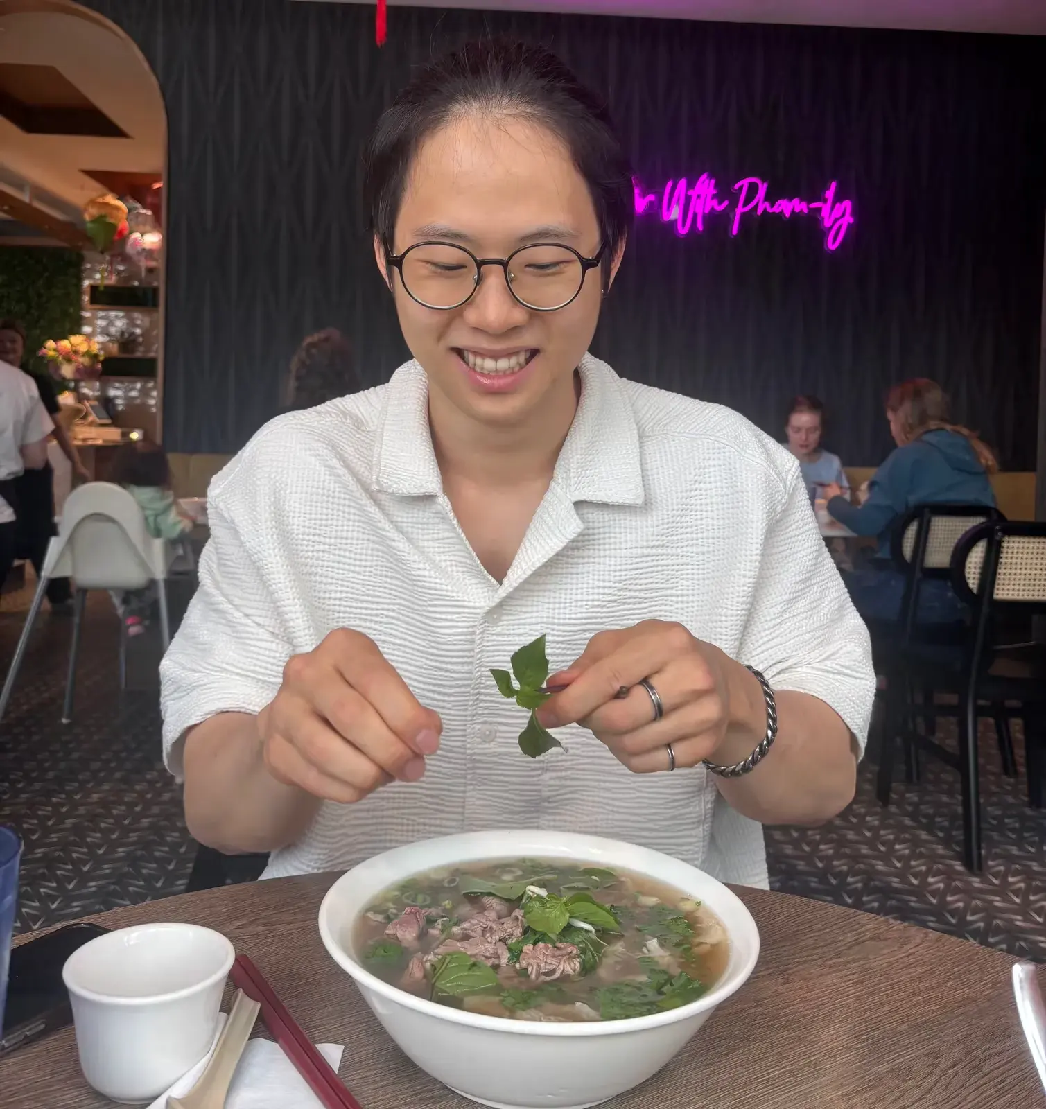 Liam adding fresh herbs to a bowl of pho at a restaurant.